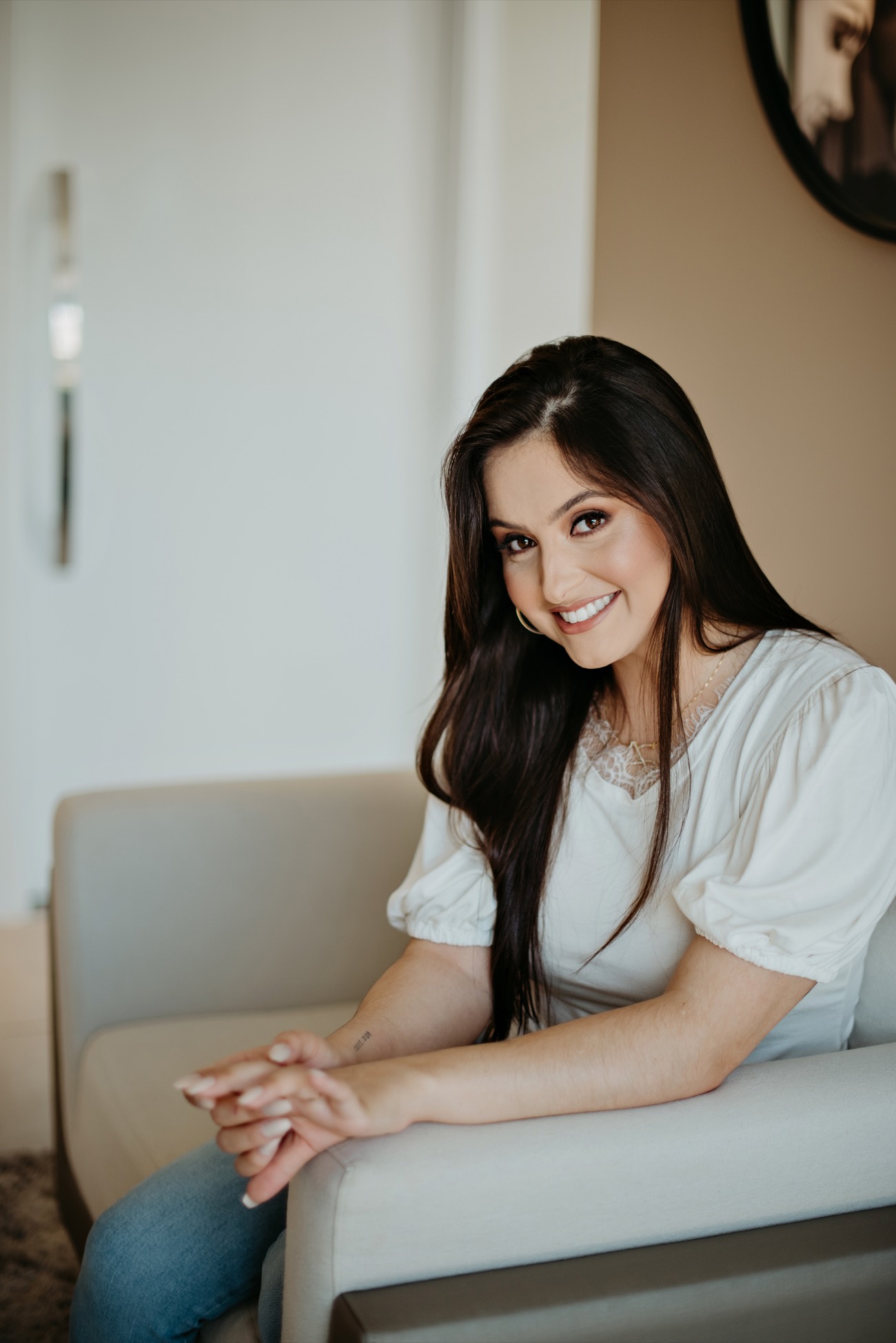 Aline Santin sorrindo, sentada em um ambiente acolhedor e iluminado